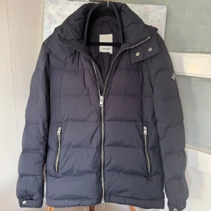 Jacka från J.Lindeberg - Säljer en snygg pufferjacka från J.Lindeberg i  bra skick. Jackan har en dragkedja framtill och två praktiska fickor med dragkedjor. Slitage på jackfickorna finns (se bilder) samt liknande slitage på luvan