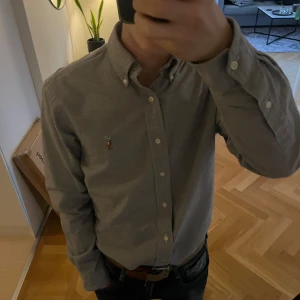 Grå ralph lauren skjorta - Säljer en stilren grå skjorta från Ralph lauren skjortan köptes för ungefär 2 månader sen, och den är använt enbart 1 gång. Hör av dig om eventuella frågor!😊