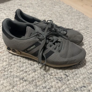 Grå Adidas sneakers - Säljer ett par grå Adidas sneakers i storlek herr 44. Skorna har en klassisk design med svarta ränder och snörning. De är perfekta för träning eller vardagsbruk. Lite slitna men fortfarande i bra skick. Passar bra till både jeans och träningskläder.
