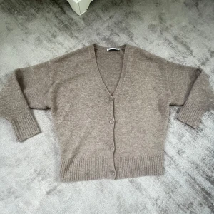 Beige kofta från Zara - Mysig beige kofta från Zara i mjukt material. Den har en v-ringad design med knappar. Perfekt till höst- och vinterdagar. 