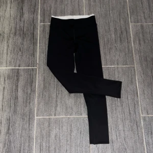 Svarta leggings från Puma - Säljer ett par svarta leggings från Puma i bra skick. De har en vit resår i midjan och Puma-loggan tryckt längs benet. Perfekta för träning eller en avslappnad dag. Superbekväma och stilrena!