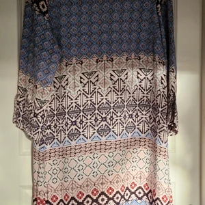 Klänning  - En fin klänning med ett mönster i blått, rosa och svart. Klänningen har en rund halsringning och tre fjärdedels ärmar. Den har en dold dragkedja i ryggen.