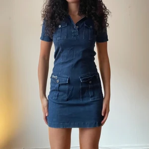 Mörkblå jeansklänning - Snygg mörkblå jeansklänning i kort modell med korta ärmar och knappar framtill. Perfekt för en avslappnad sommarlook eller en dag på stan. Klänningen har praktiska fickor och en figurnära passform som framhäver silhuetten.