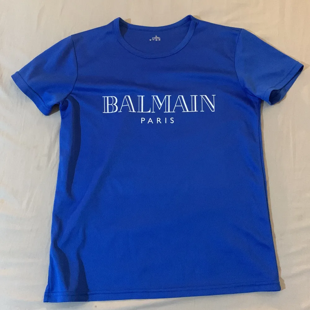 Snygg blå t-shirt från Balmain med deras ikoniska logga i vitt på bröstet. Perfekt för en casual look eller att klä upp med en kavaj. Gjord i mjukt material för en bekväm passform. Ett måste för alla modeälskare!. T-shirts.