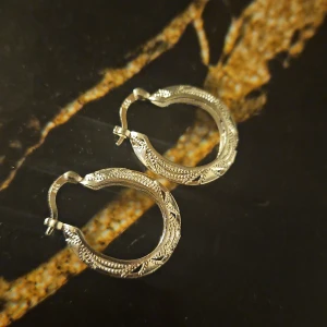 Silver örhängen med mönster - Säljer ett par snygga silver örhängen med detaljerat mönster. De är i form av små ringar och har en klassisk stil som passar perfekt till både vardag och fest. Örhängena är i nyskick och redo att bäras av någon som älskar stilrena smycken.