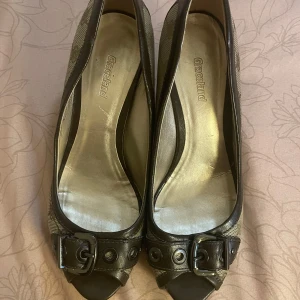 Bruna pumps  - Snygga bruna pumps i storlek 37 från Graceland med öppen tå och dekorativa spännen framtill. Skorna har ett diskret rutigt mönster i beige och svart, vilket ger dem en elegant touch. Perfekta för både fest och vardag!