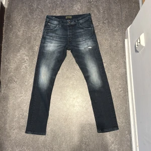 Mörkgrå jeans från Jack & Jones - Säljer ett par snygga mörkblå jeans från Jack & Jones. De har en slim fit och är i mycket bra skick. Jeansen har en klassisk femficksdesign och en lätt slitning på framsidan för en cool look. Minimal fläck på båda knän. Annars fantastiskt skick!