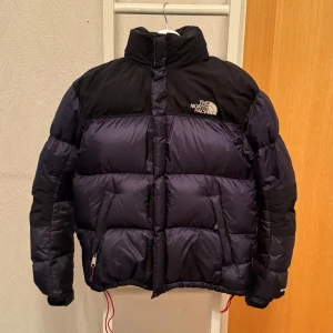 The North Face vintage jacka - varm dunjacka från The North Face Summit Series. Den är svart och mörkblå. Perfekt för kalla vinterdagar. Jackan har en pufferstil och är i mycket bra skick. Passar både till vardags och utomhusaktiviteter.
