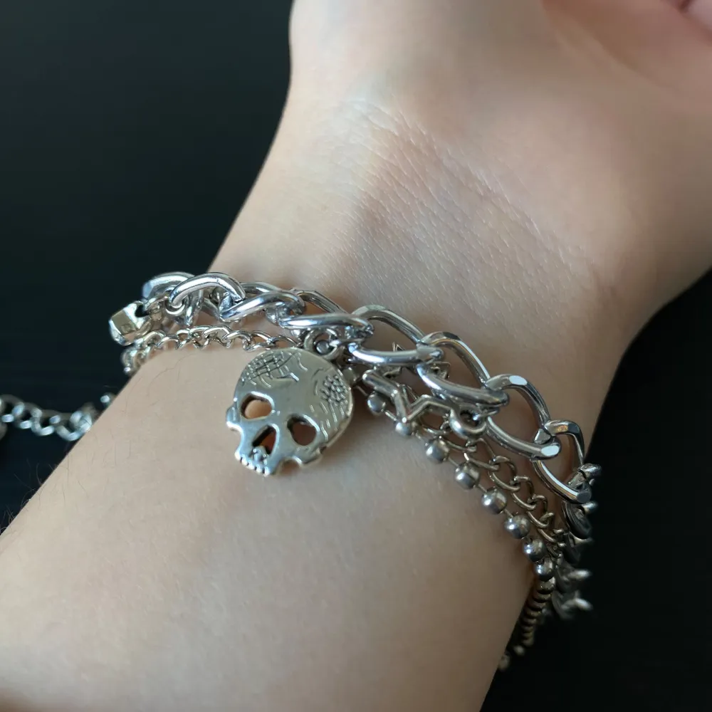 Coolt silverfärgat armband med flera kedjor och unika berlocker som en dödskalle, stjärnor, vingar och en tand. ca 16 cm och kan justeras upp till 20 cm! Perfekt för att ge din outfit en edgy touch. Armbandet har en justerbar kedja för att passa olika storlekar. Passar perfekt till både vardag och fest!. Accessoarer.