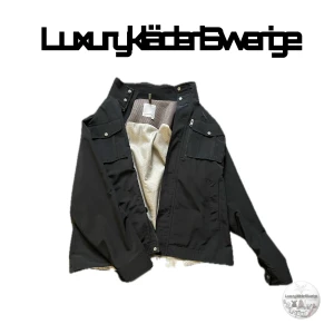 Svart jacka från J.Lindeberg - Säljer en snygg svart jacka från J.Lindeberg i storlek L/XL. Jackan är tillverkad i 100% polyester och har en stilren design med dragkedja och knappar. Perfekt för höst och vår med sina praktiska fickor och bekväma passform.Ny pris 3400.  För mer information dm✉️