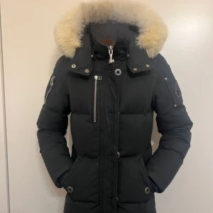 Moose Knuckles Jacka - Säljer en snygg svart dunjacka från Moose Knuckles med fluffig päls på huvan. Jackan har en cool design med dragkedja och knappar, samt praktiska fickor. Perfekt för kalla vinterdagar. Såklart är den äkta. Skriv gärna till om du har några frågor. NFC finns som äkthets bevis. 