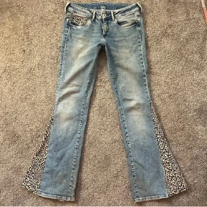 Blå jeans med leoparddetaljer - Säljer ett par unika blå jeans med leopardmönstrade detaljer på fickor och längs benen. De har en bootcut-stil som ger en cool retrovibe. Perfekta för att sticka ut i mängden! 🐆