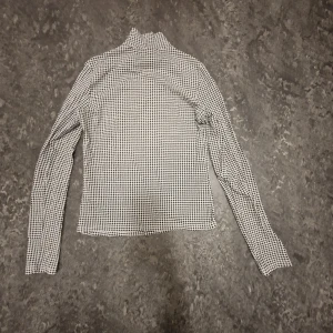Svartvit polotröja från Monki - Säljer en snygg svartvit polotröja från Monki i storlek XS. Tröjan har ett klassiskt hundtandsmönster och är perfekt för både vardag och fest. Den är långärmad och gjord i ett mjukt material som känns skönt mot huden. Perfekt för höst och vinter!