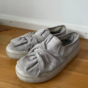 Grå mocka sneakers med knyt - Säljer ett par grå sneakers i mocka med en unik knytning på ovansidan. De har en chunky sula och ser riktigt bekväma ut. Perfekta för en avslappnad stil men ändå med en twist. Använda men i bra skick.