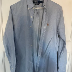 Blå skjorta från Polo Ralph Lauren - Säljer en snygg blå skjorta från Polo Ralph Lauren i storlek S. Skjortan har en slim fit passform och är långärmad med klassiska knappar. Perfekt för både vardag och festliga tillfällen. Den har en liten broderad logga på bröstet som ger en stilren touch. Passar perfekt till både jeans och chinos!