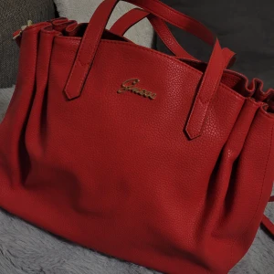 Röd axelväska från Guess - Säljer en snygg röd axelväska från Guess i mycket bra skick. Väskan är gjord av skinn och har en praktisk dragkedja upptill. Perfekt för både vardag och fest! 🌸😊❤️ (priset kan sänkas om önskat)