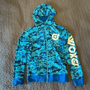 Blå camo hoodie från Woxo - Säljer en cool blå camo hoodie från Woxo. Den har en dragkedja framtill och en stor logga på ärmen. Perfekt för höst och vår, med en skön passform och ribbade muddar. Grym för både chill och aktivitet! 💙