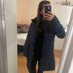 Mörkblå ridjacka från CRW - Säljer en snygg och varm mörkblå dunjacka från CRW. Perfekt för kalla vinterdagar med sin långa design och dragkedja framtill. Jackan har en huva och är i mycket bra skick. Passar perfekt för både ridning och utomhusaktiviteter.