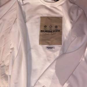 Säljer en stilren vit långärmad tröja från Burberry. Den har en beige patch med Burberry-loggan på bröstet och en diskret broderad detalj på ärmen. Perfekt för både vardag och fest. Passar bra till jeans eller chinos för en avslappnad men ändå elegant look. Priset går och diskuteras 😊