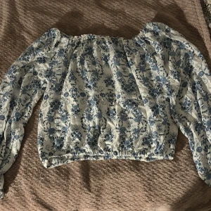 Blommig offshoulder topp från KappAhl - Säljer en superfin blommig offshoulder topp från KappAhl i storlek 158/164. Den är vit med blå blommönster och har långa ärmar.🩷