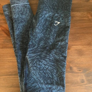 Mönstrade leggings från Gymshark - Säljer ett par snygga mönstrade leggings från Gymshark i storlek S. De är i en blå/turkos nyans med ett coolt mönster och har en tight passform. Perfekta för träning eller en avslappnad dag. Superbekväma och stiliga!