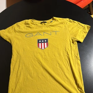 Gul t-shirt från GANT - Säljer en snygg gul t-shirt från GANT med korta ärmar och ett coolt tryck på framsidan. Perfekt för sommardagar eller avslappnade tillfällen. T-shirten är i bra skick och gjord av mjukt bomullsmaterial.