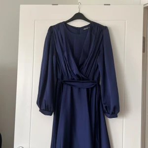 Marinblå långklänning från Turkiet   - Elegant marinblå långklänning från Turkiet i ett mjukt och flödande material. Klänningen har långa ärmar och en v-ringad omlottdesign som ger en stilren look. Perfekt för höst- och vinterfester eller en formell tillställning. Den har en markerad midja som framhäver figuren.