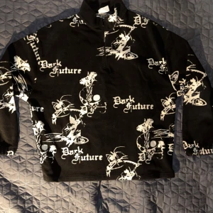 Svart fleece tröja från ASOS Design - Säljer en cool svart fleece tröja från ASOS Design med trycket 'Dark Future' i vitt. Tröjan har en halv dragkedja och är perfekt för kyliga dagar. Den är både bekväm och stilren, perfekt för en avslappnad look.