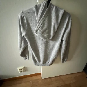 Grå hoodie från Umbro - Säljer en grå hoodie från Umbro i mycket bra skick. Den har en stor logga på framsidan och en praktisk magficka. Perfekt för höst och vinter, eller bara för att chilla hemma. Storleken är normal och materialet känns mjukt och skönt.