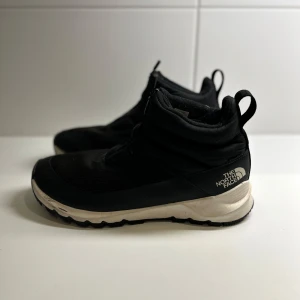 Svarta vinterstövlar från The North Face - Säljer ett par svarta vinterstövlar från The North Face i mycket bra skick, storlek 41. Använt ett fåtal gånger. De har en robust sula och är perfekta för kalla dagar. Skorna är vadderade för extra värme och komfort. Perfekta för vinterns äventyr!