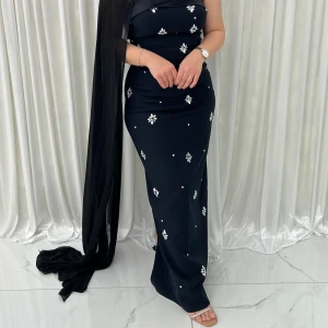 Svart midiklänning - Elegant svart midiklänning med en axelbandslös design. Klänningen har en slits baktill och ett vackert draperat tyg över ena axeln. Perfekt för festliga tillfällen! Använd endast en gång och är i utmärkt skick! Storlek 40 men funkar även på en 38:a. Jag är 158 cm och bär klack på 5 cm.