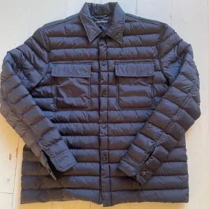 Mörkblå pufferjacka från J.Lindeberg - Säljer en snygg mörkblå pufferjacka från J.Lindeberg i storlek M. Jackan är i mycket bra skick och perfekt för höst och vinter. Materialet är 100% polyester vilket gör den både lätt och varm. Perfekt för kyliga dagar! Orginal pris: 3200kr 