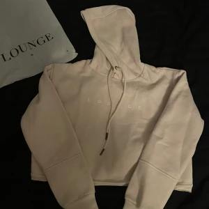 Beige kort huvtröja från Lounge Oanvänd - Säljer en supermysig beige hoodie från Lounge i storlek XS. Den är croppad och har en stor luva med dragsko. Helt ny och oanvänd, kommer i originalförpackning.