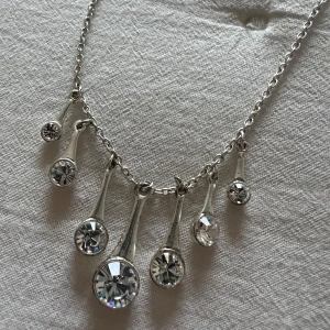 Silverfärgat halsband från Pilgrim - Snyggt silverfärgat halsband från Pilgrim med flera droppformade hängen prydda med glittrande stenar. Perfekt för att ge en elegant touch till din outfit. Kedjan är justerbar för att passa olika längder. Ett måste för smyckesälskare! ✨