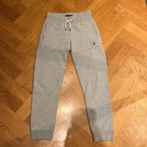 Grå mjukisbyxor från Tommy Hilfiger - Säljer ett par grå mjukisbyxor från Tommy Hilfiger i storlek 140. De har en bekväm passform med snörning i midjan och ribbade muddar vid bensluten.  Byxorna har också det klassiska Tommy Hilfiger-logotypen på sidan. Supermjuka och sköna! 