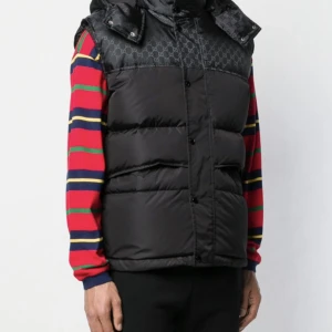 Svart dunväst med mönster - Säljer en snygg svart dunväst med diskret mönster. Västen har knappar och en hög krage för extra värme. Perfekt för höst och vinter, och funkar både till vardags och fest. Passar bra över en färgglad tröja för en cool look. Storlek är medium endast seriösa 