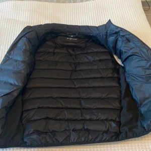 Svart dunväst från Sail Racing spray down vest  - Säljer en snygg svart dunväst från Sail Racing i storlek medium. Perfekt för höst och vår, med en stilren design och dragkedja framtill. Västen är quiltad och håller dig varm utan att vara för tung. Passar både till vardags och lite mer uppklädda tillfällen.