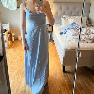 Ljusblå långklänning från NA-KD - Säljer en superfin ljusblå långklänning från NA-KD. Den har smala axelband och en snygg öppen rygg med knytning. Perfekt för bal som jag använt den till. Klänningen är i ett mjukt och skönt material som faller fint. Storlek 38