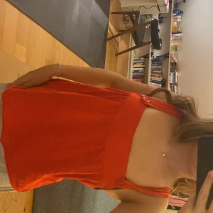 Röd topp - Säljer en snygg röd topp med breda axelband och knappliknande detaljer. Perfekt för sommardagar eller en kväll ute. Toppen har en luftig passform och är superbekväm att bära. Passar bra till både jeans och kjol!