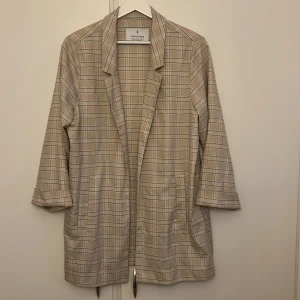 Beige rutig kavaj från Stradivarius - Säljer en snygg beige rutig kavaj från Stradivarius . Den har trekvartsärmar och en avslappnad passform, perfekt för både vardag och fest. Kavajen har en klassisk krage och två fickor framtill. Superfin att matcha med jeans eller klänning!