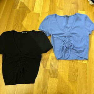 Svart och blå ribbad topp från Zara - Två snygga ribbade toppar från Zara i svart och blått. De har en v-ringad design med knytning framtill som ger en cool look. Perfekta för både vardag och fest! 🖤💙