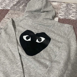 CDG kofta - Säljer en snygg grå hoodie från Comme des Garçons med det ikoniska hjärtat med ögon på ryggen. Den är jätte bekväm och är i nytt skick.