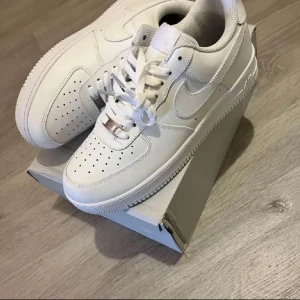 Vita Nike Air Force 1 - Säljer ett par klassiska vita Nike Air Force sneakers i nytt skick. De har en stilren design med snörning och är perfekta för vardagsbruk. Skorna är i storlek 42 och kommer i originalkartong. Passar till alla outfits och är superbekväma!