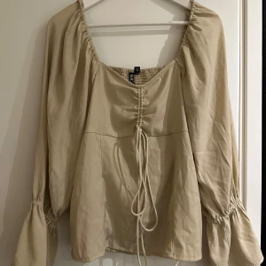 Beige långärmad topp från Pieces - Säljer en superfin beige långärmad topp från Pieces i storlek XL. Helt oanvänd, endast testad. Toppen har en snygg knytning framtill och är gjord i 100% polyester. Perfekt för både vardag och fest! 💫