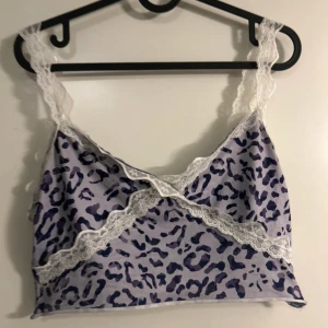 Lila leopardmönstrad topp med spetsdetaljer - Säljer en superfin leopardmönstrad linne i lila och vit med spetsdetaljer. Toppen är ärmlös och har en v-ringad design med spets längs kanterna. Perfekt för en festlig kväll eller bara för att känna sig extra snygg!💜