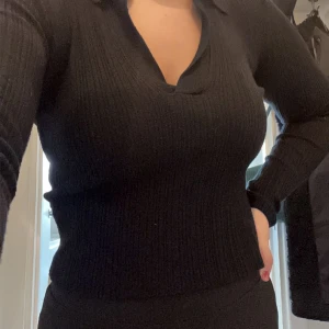 Svart ribbad tröja - Säljer en stilren svart ribbad tröja med v-ringning. Perfekt för både vardag och fest. Tröjan har långa ärmar och en skön passform som sitter snyggt på kroppen. Passar till alla tillfällen!