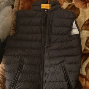 Parajumper väst - En snygg och stilren väst från Parajumpers. Västen har en hög krage och en dragkedja framtill. Den har två fickor på framsidan och en ficka på insidan. Västen är i gott skick och har inte använts mycket.