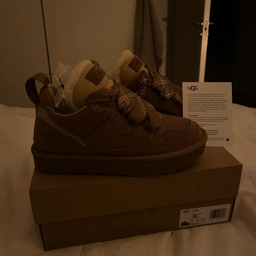 Säljer ett par snygga bruna sneakers från UGG i nytt skick. De har en mysig pälsfodring och breda snören för extra stil. Perfekta för höst och vinter med sin varma design.  Kommer i originalkartong. Modellen heter Lowmel från märket UGG. Skorna är helt nya och aldrig använda . Skor.