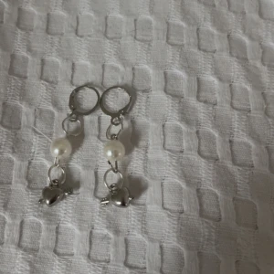Söta örhängen med pärlor och hjärtan -  (Endast Swish) Charmiga örhängen med vita pärlor och små silverfärgade hjärtan. Perfekta för att ge en romantisk touch till din outfit. Passar både till vardags och festliga tillfällen. 💖
