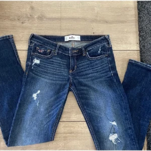 Mörkblå jeans med slitningar - Säljer ett par snygga mörkblå jeans från Hollister. De har coola slitningar och en låg midja med raka ben. Perfekta för en casual outfit!